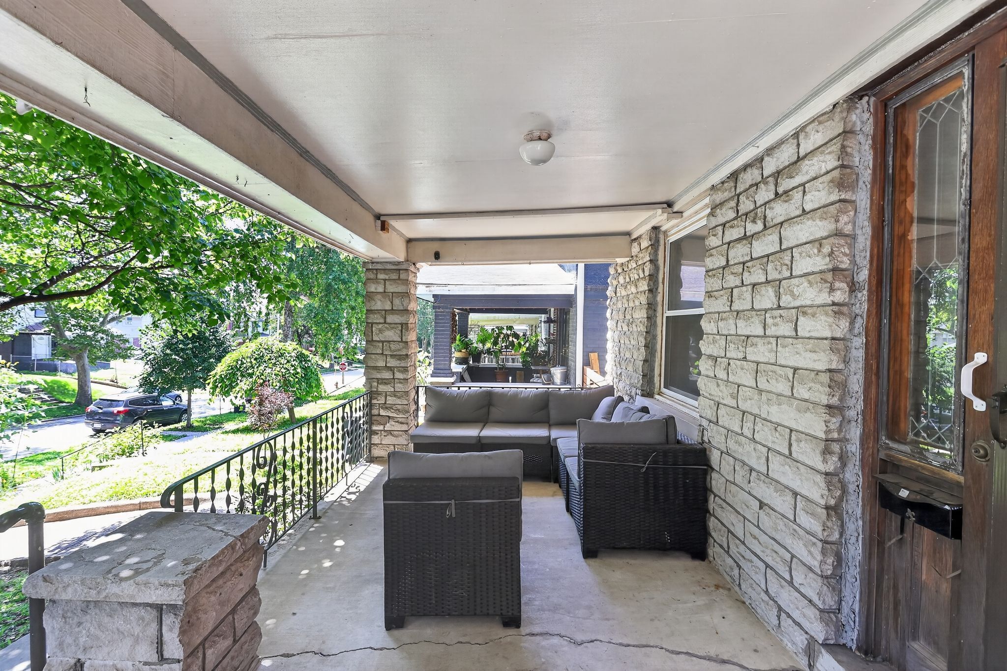 A covered porch with outdoor seating, a stone wall, and a view of the street.