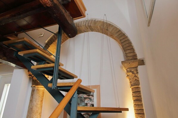 Eine Wendeltreppe mit Holzstufen und Metallgeländern, die zu einem steinernen Bogen führt.