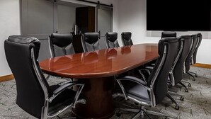 Una sala de conferencias con una gran mesa ovalada, sillas de cuero negro, un televisor de pantalla plana grande y un separador de vidrio.