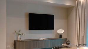 Ett modernt vardagsrum med en platt-TV som är monterad på väggen, en sidobord med en lampa och ett matbord med stolar.