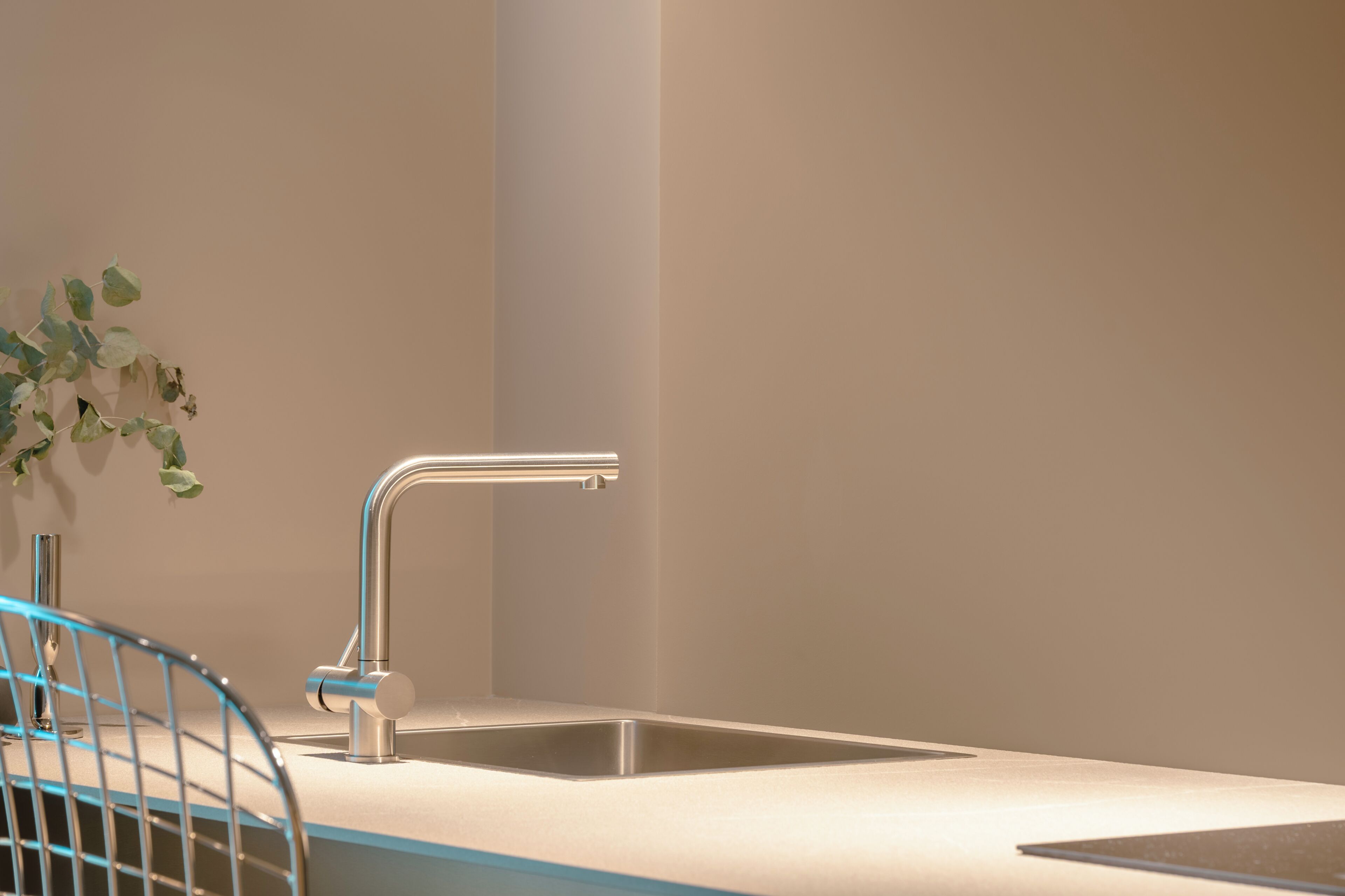 A modern kitchen with a stainless steel sink, a blue chair, and a potted plant.