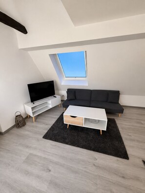 Ein modernes Wohnzimmer mit einem Flachbildfernseher, einem schwarzen Sofa, einem weißen Couchtisch und einem Oberlicht.
