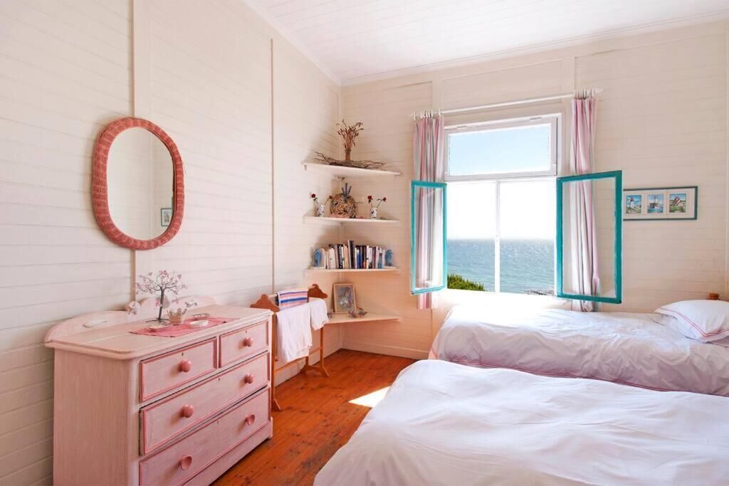 A bedroom with a bed, a dresser, a desk, shelves with books and decorations, and a window with curtains.