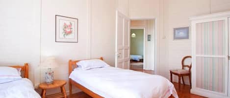 Un dormitorio con dos camas individuales, una silla de madera, una mesita con lámpara y un armario.