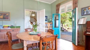 A dining area with a wooden table and chairs, a vase with flowers, and a view of the outdoors through a door. - Stunning Boulders Beach house  (Simons Town, Cape Town)