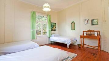 Une chambre avec deux lits, une table en bois et une fenêtre avec des rideaux.