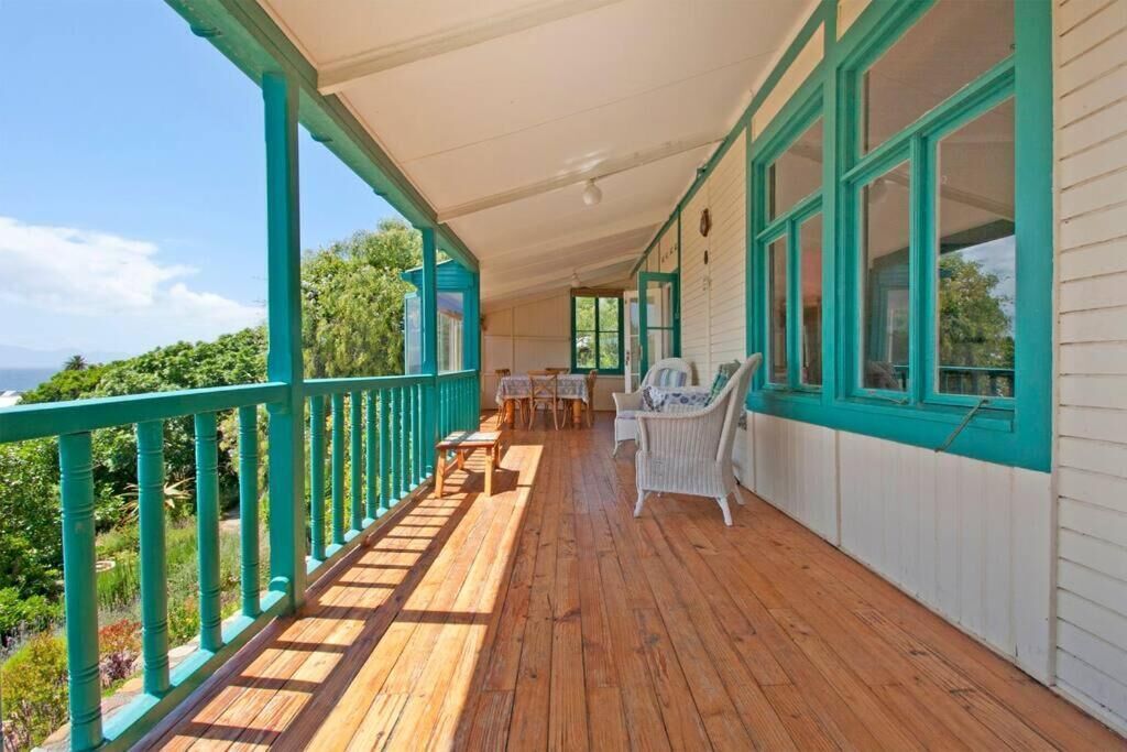 Eine überdachte Veranda mit Holzboden, weißen Wänden mit türkisblauen Akzenten und Blick ins Grüne.