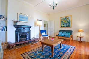 Un salón con chimenea, un sillón azul, un sofá, una mesa de centro de madera y una alfombra estampada.
