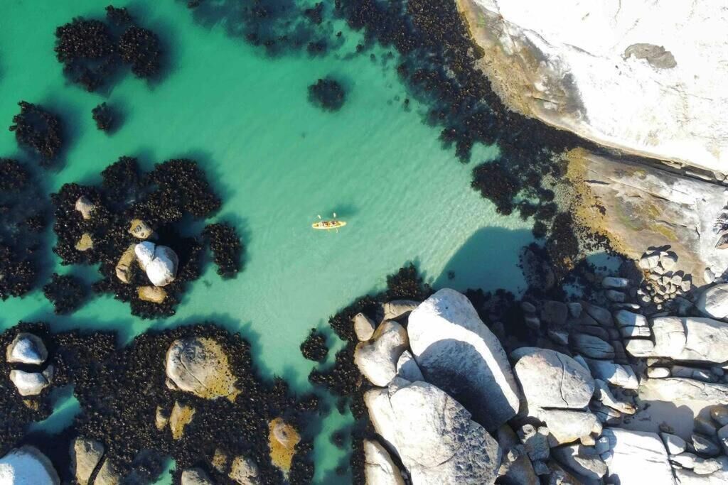 An aerial view of a coastal area with clear turquoise water, rocky formations, and a small boat.