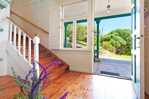 Una scala in legno con ringhiere bianche che conduce a una stanza con vista su un giardino attraverso una porta in vetro.