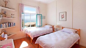 A bedroom with two beds, a window with curtains, a shelf with books, and a framed picture on the wall. - Stunning Boulders Beach house  (Simons Town, Cape Town)