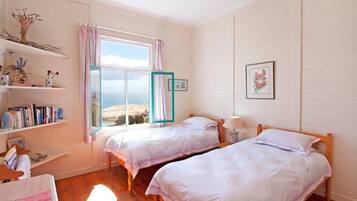 A bedroom with two beds, a window with curtains, a shelf with books, and a framed picture on the wall.