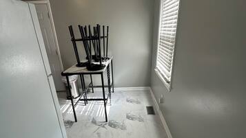 Une petite cuisine avec un sol en marbre, une table à manger avec des chaises, une fenêtre avec des stores et une porte blanche.