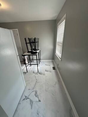 A small kitchen with a marble floor, a dining table with chairs, a window with blinds, and a white door.