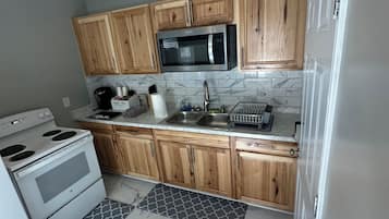 Une cuisine compacte avec des meubles en bois, un four à micro-ondes en acier inoxydable, une cuisinière et un pare-feu en marbre.