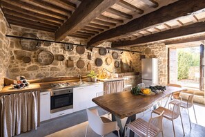 A rustic kitchen with stone walls, wooden beams, and a large wooden table with chairs. - Villa Bastia by MMega (San Leo Bastia)