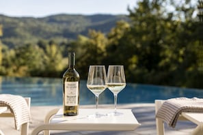 Eine Flasche Torre di Giano Wein und zwei Gläser auf einem Tisch am Pool mit Blick auf Hügel.