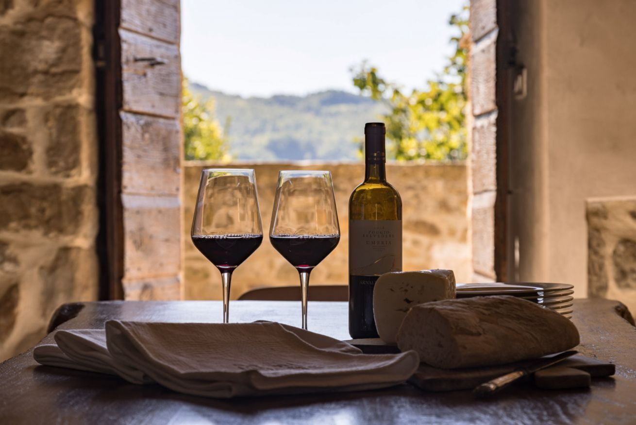 A table with two wine glasses, a bottle of wine, cheese, and a knife. - Villa Bastia by MMega (San Leo Bastia)