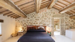 A bedroom with a stone wall, a wooden ceiling, a bed, a bedside table, and a nightstand. - Villa Bastia by MMega (San Leo Bastia)