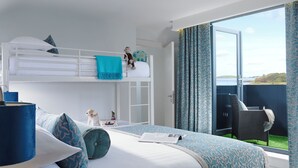Habitación de hotel con literas, un balcón con vistas y una zona de estar con mesa.