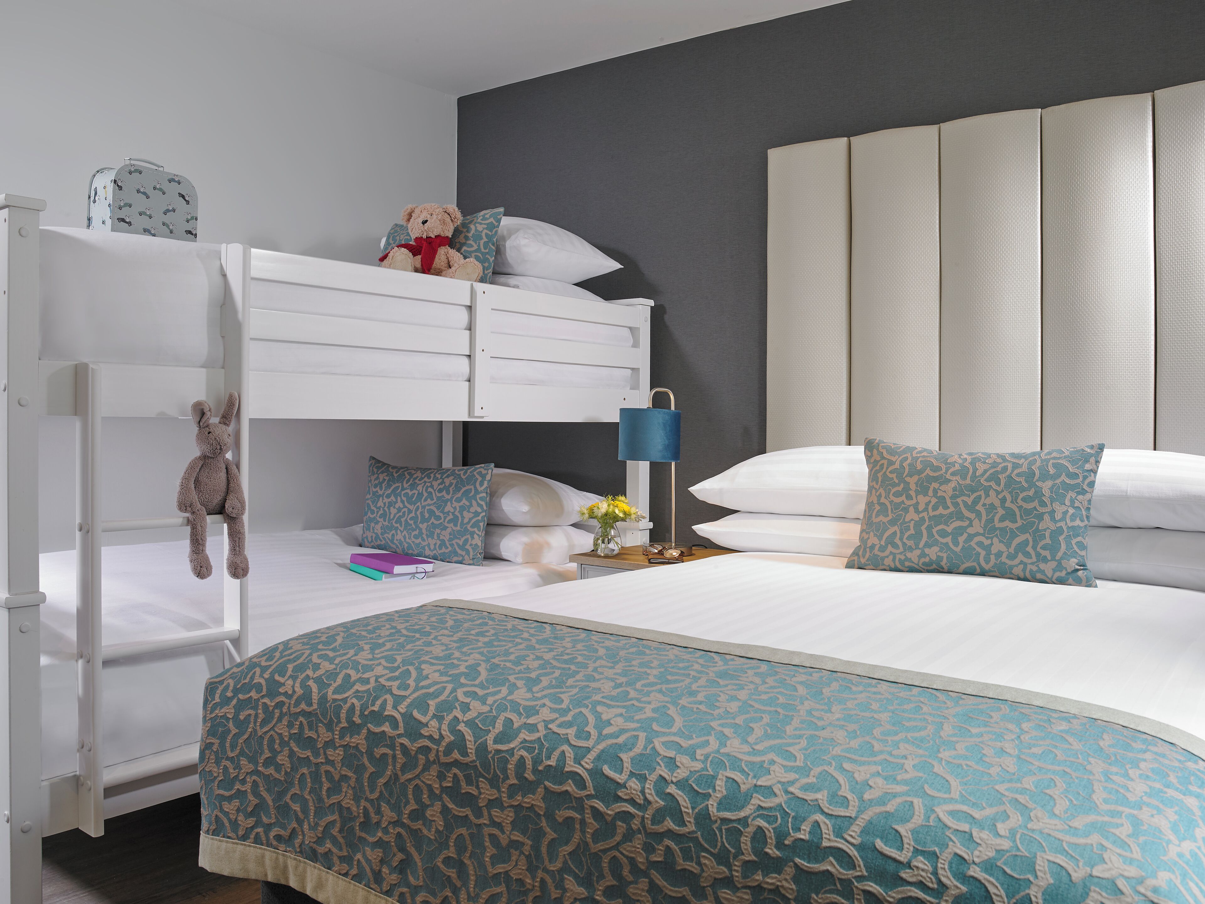 Une chambre avec des lits superposés, une table de chevet avec une lampe et des coussins décoratifs.