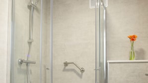 Un baño moderno con ducha de vidrio, inodoro blanco y un pequeño florero con flores en un estante.