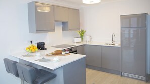 Una cocina moderna con armarios grises, horno empotrado, refrigerador y una zona de comedor con una silla y mesa.