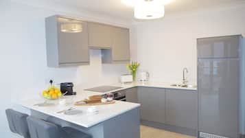 A modern kitchen with grey cabinets, a built-in oven, a refrigerator, and a dining area with a chair and table.