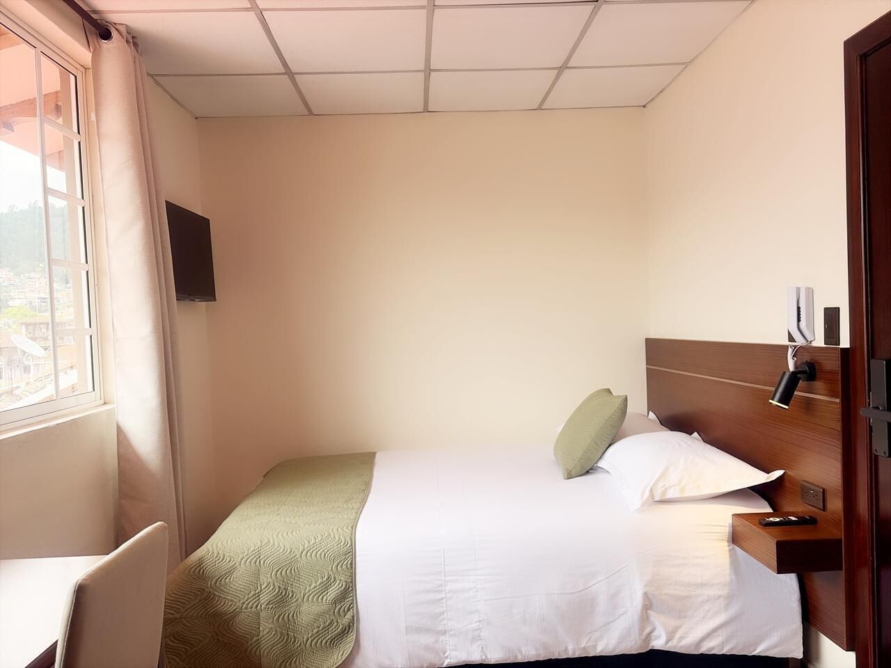 Ein Hotelzimmer mit Bett, Nachttisch, Lampe und einem Fenster mit Vorhängen.