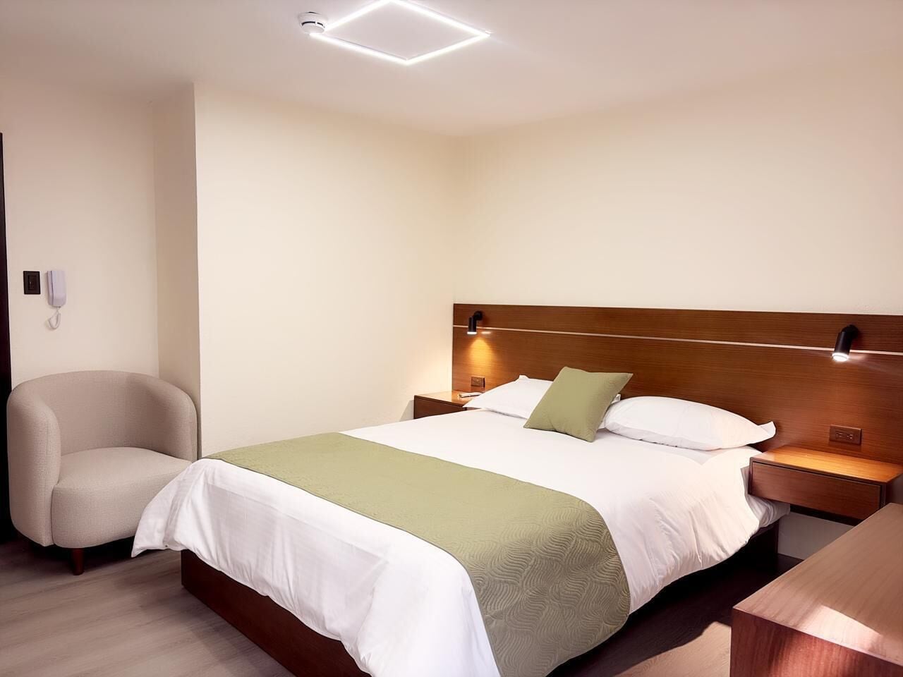 A hotel room with a bed, bedside tables, a chair, and a wall-mounted phone.