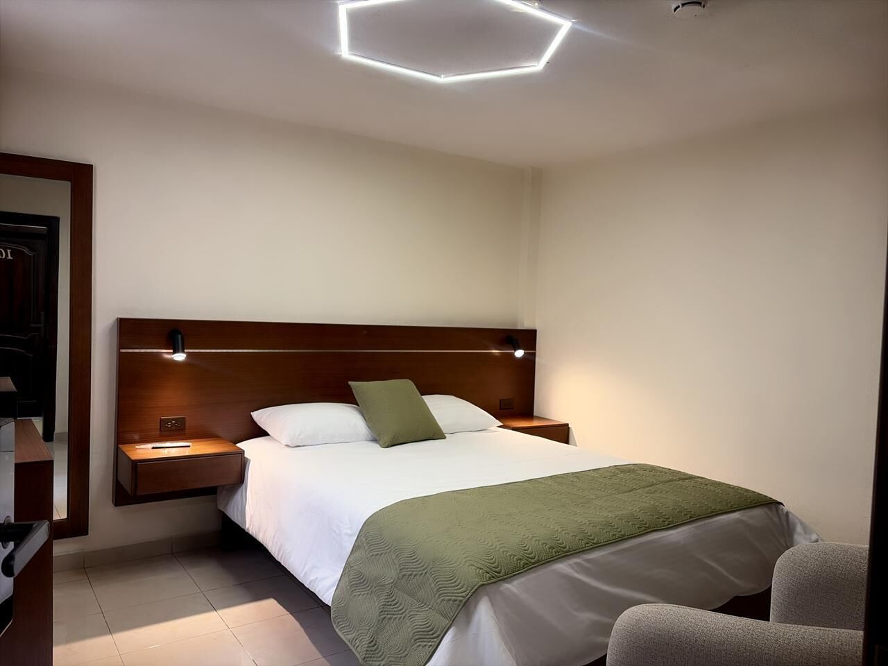A hotel room with a bed, bedside tables, a nightstand, and a modern ceiling light fixture.