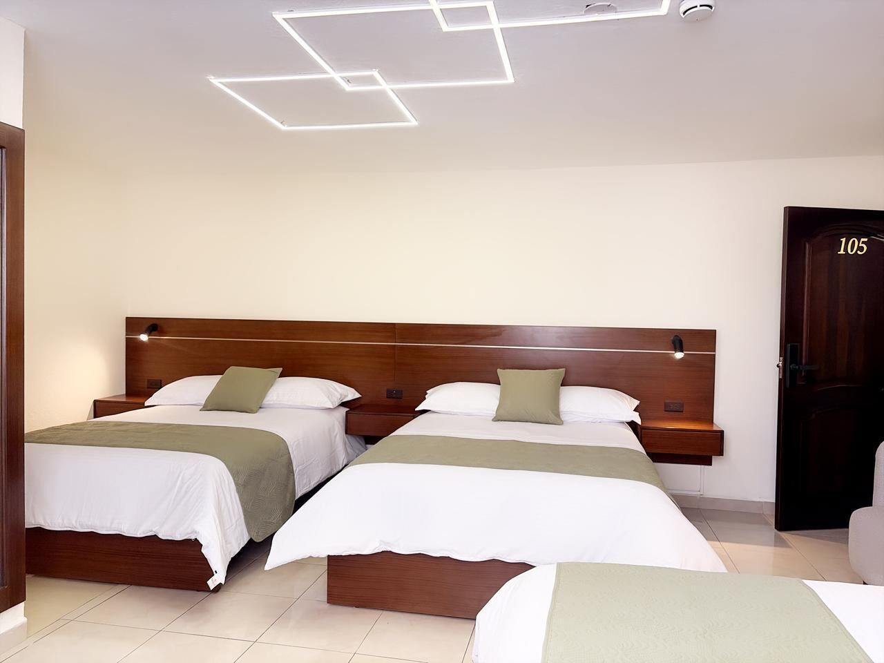 Ein Hotelzimmer mit zwei Betten, Holz-Kopfteilen, Nachttischen und einer Tür mit der Nummer 105.