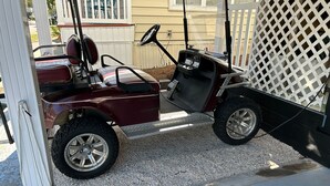 Um carrinho de golfe cor de vinho com volante e assento, estacionado em uma entrada de cascalho.