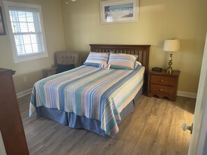 Ein Schlafzimmer mit Bett, Stuhl, Nachttisch, Lampe und Fenster.