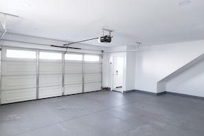 Eine geräumige Garage mit weißen Garagentüren, einem an der Decke befestigten Projektor und einer Tür zu einem weiteren Raum.