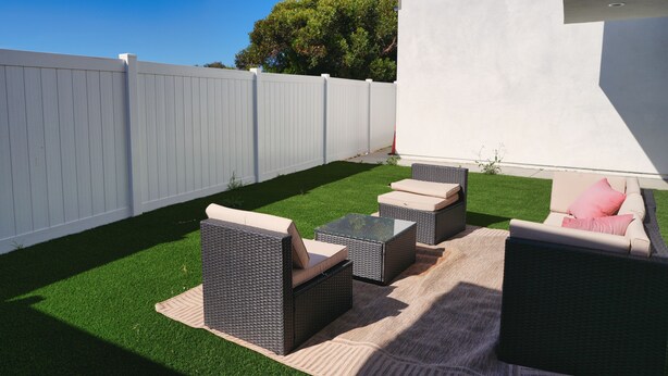 A backyard with artificial grass, wicker furniture, and a white fence. - Spacious Central San Diego Home! (San Diego)