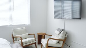 A modern room with a bed, two armchairs, a small round table, and a mounted TV. - Spacious Central San Diego Home! (San Diego)