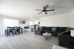 Ein modernes Wohnzimmer mit grauem Sofa, Couchtisch und einem Essbereich mit Stühlen und Tisch.