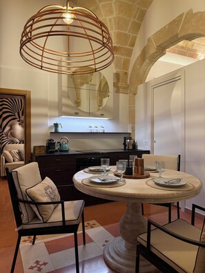 A dining area with a round table set for four, a modern pendant light, and a stone archway in the background. - Angel Apartments by Monholiday (Monopoli)