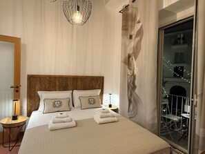 A hotel room with a large bed, two pillows, a wooden headboard, a bedside table with a lamp, and a view of a balcony with lights. - Angel Apartments by Monholiday (Monopoli)
