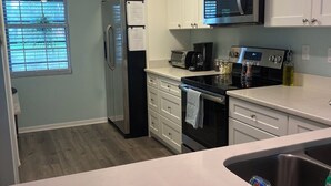 Eine moderne Küche mit weißen Schränken, einem Edelstahl-Kühlschrank, einer Mikrowelle, einem Toaster und einem Herd.