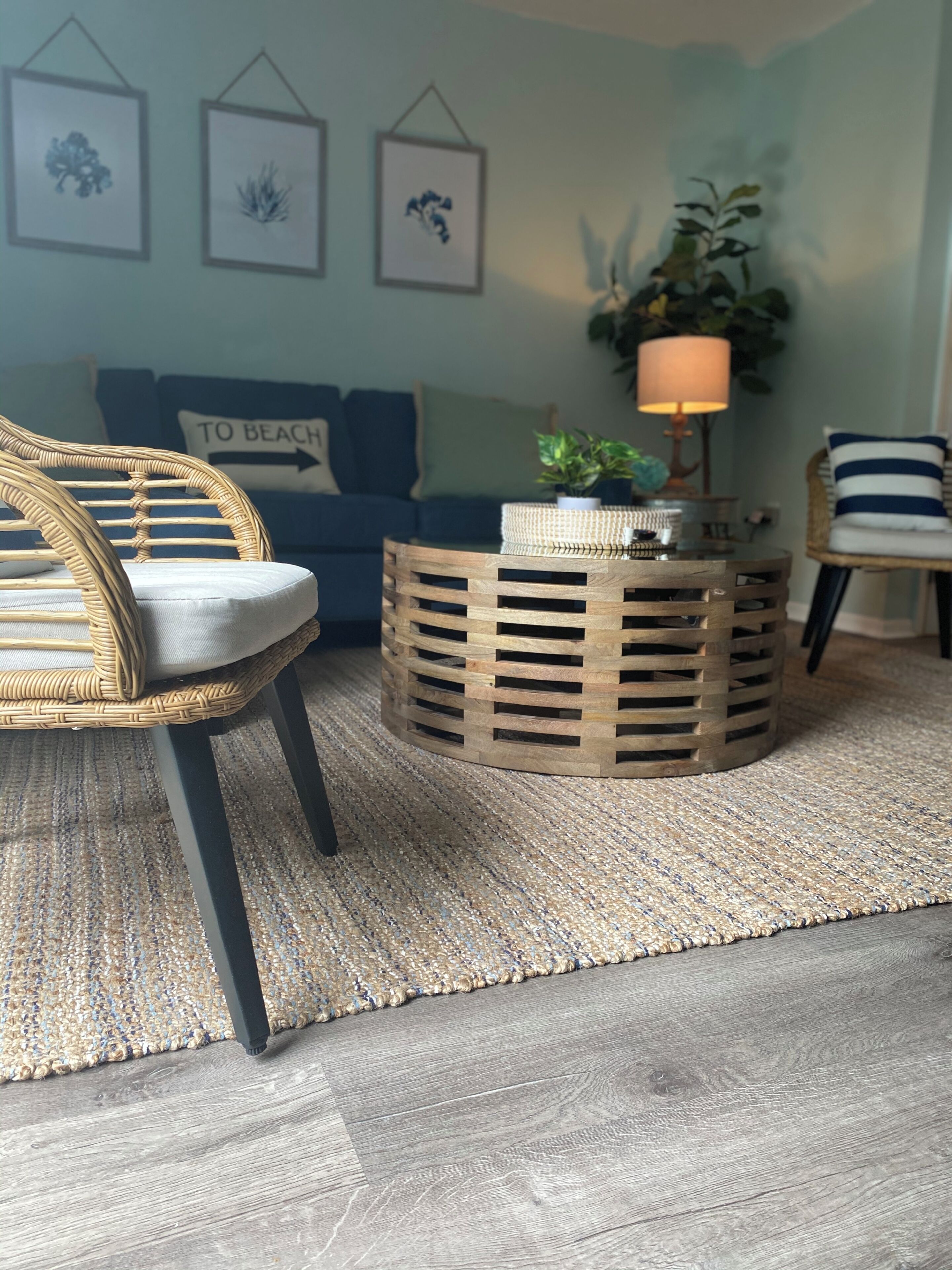 A living room with a wicker chair, a round wooden coffee table, a blue sofa, and a wall with framed artwork.