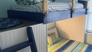 Ein Stockbett mit Schreibtisch und Leiter, eine gestreifte Bettdecke und ein Kissen mit Muster.