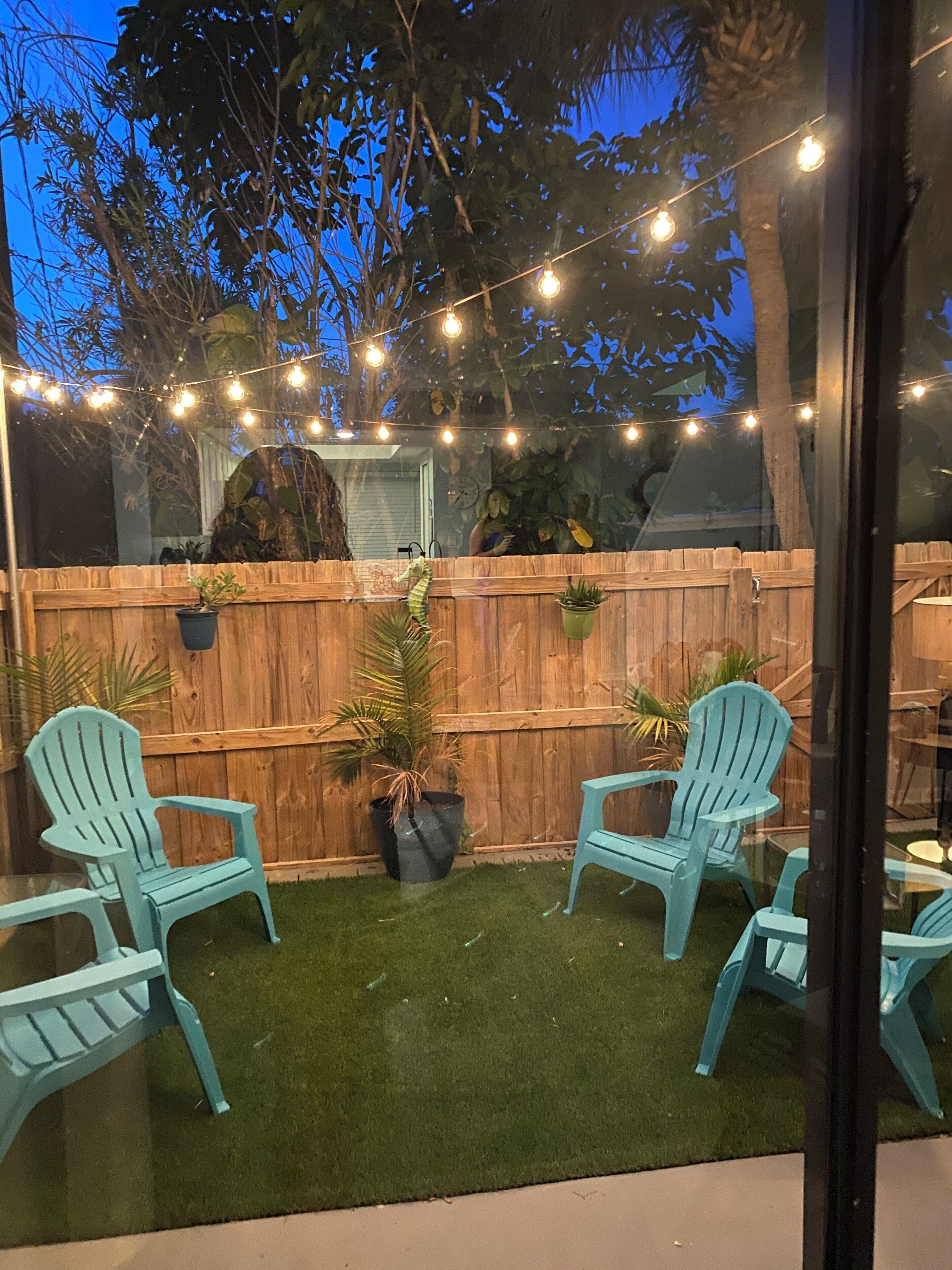 A backyard with a wooden fence, two blue chairs, and string lights.