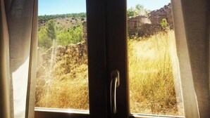 A window with a view of a natural landscape, including a stone wall and dry grass. - A cozy and unique patio overlooking the ocean (FITOU)