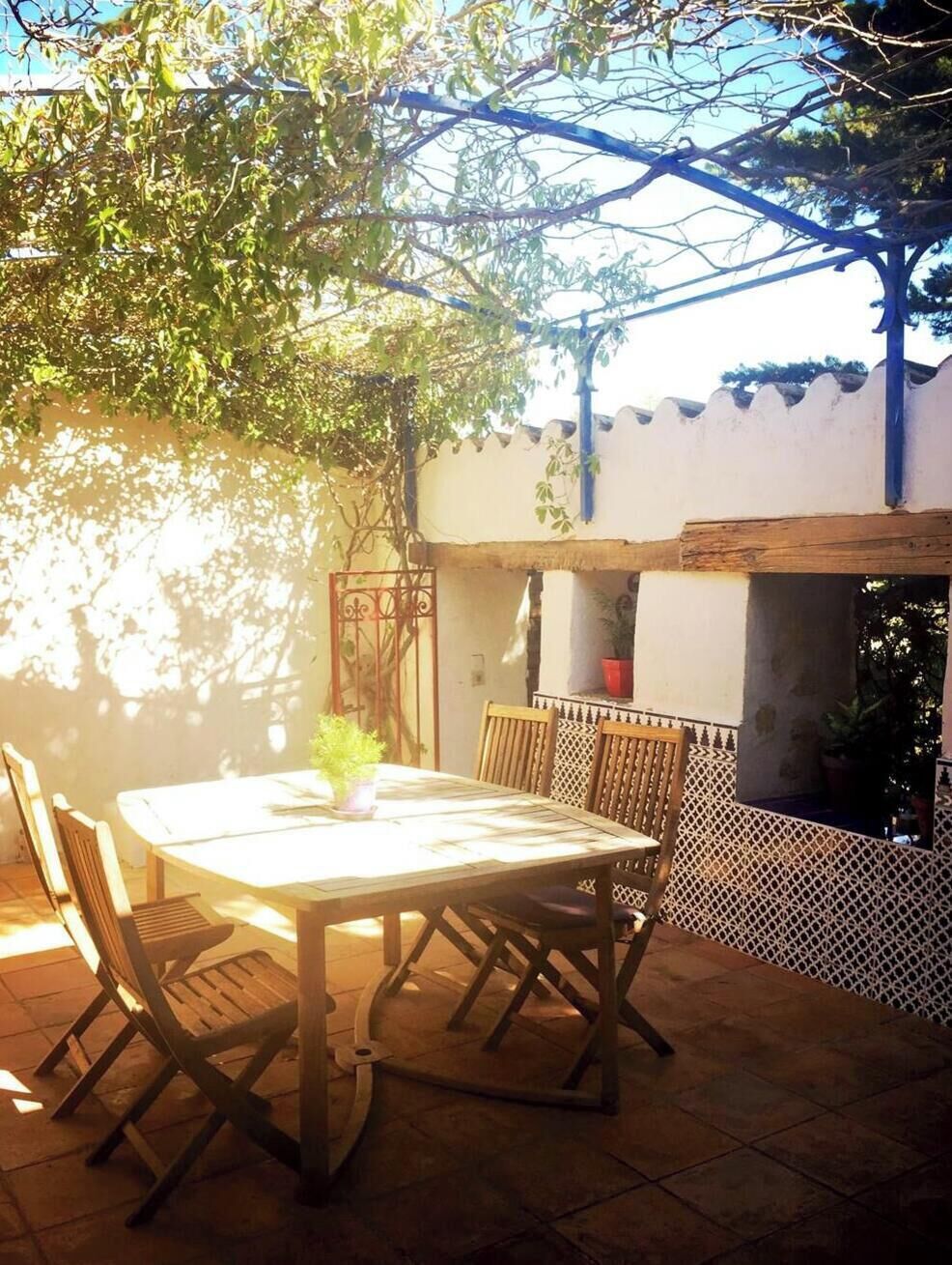 Eine Terrasse im Freien mit Tisch und Stühlen, umgeben von einer weißen Mauer mit dekorativem Muster und einer Holzw pergola darüber.