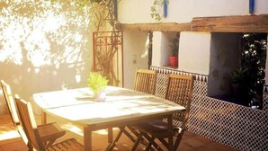 An outdoor patio with a table and chairs, surrounded by a white wall with a decorative pattern and a wooden pergola overhead. - A cozy and unique patio overlooking the ocean (FITOU)