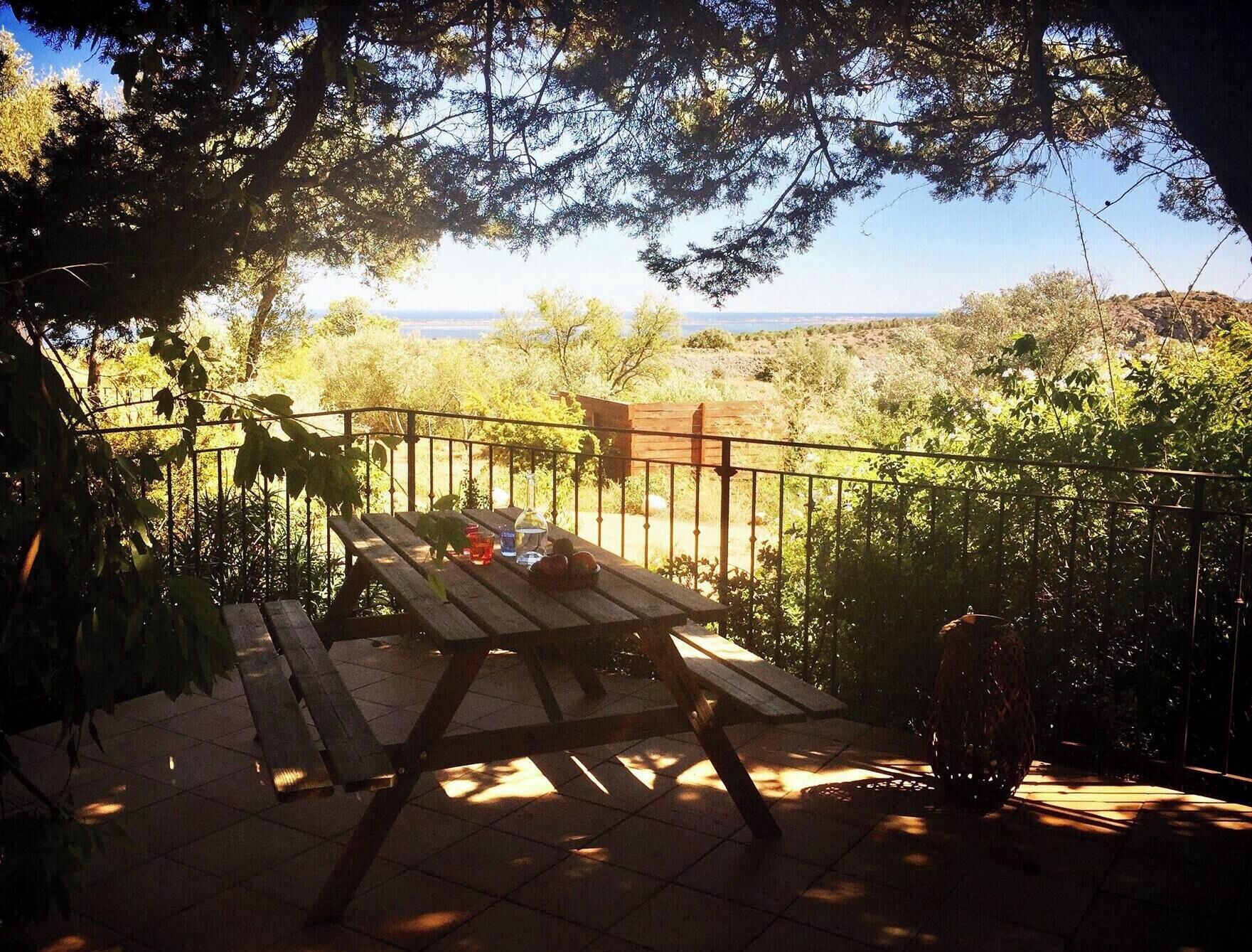 Eine Terrasse im Freien mit einem Holztisch und Bänken, umgeben von viel Grün und Blick auf die Landschaft.