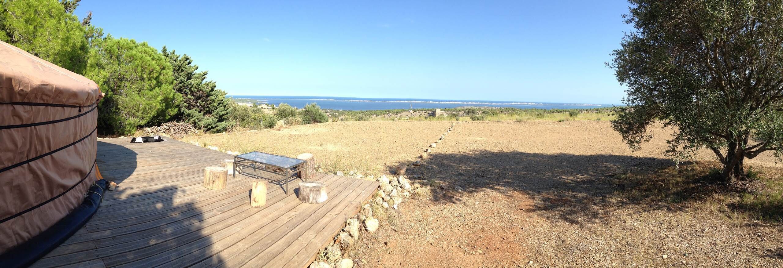 A wooden deck with a tent, a table, and a view of the sea.