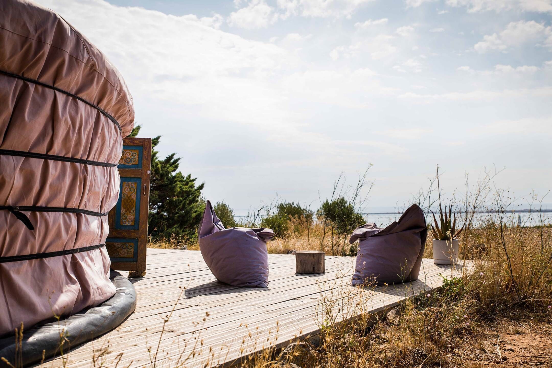 Een houten terras met twee zakkenstoelen en een groot overdekt object, waarschijnlijk een sauna, met uitzicht op zee.